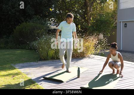 Couple afro-américain en tee et short se préparant sur une terrasse en bois en posant des tapis verts et une bouteille Banque D'Images