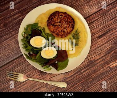 Une galette de viande frite avec de la purée de pommes de terre, des feuilles de laitue et un œuf de poulet durci sur une table en bois. Vue de dessus, flat lay. Banque D'Images