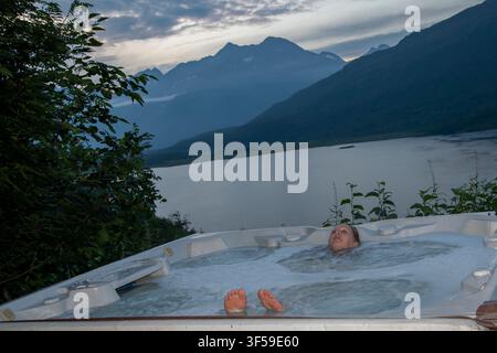 Valdez, Alaska. Une femme se détend dans un bain chaud le soir en surplombant le lac Robe pendant ses vacances en Alaska. Banque D'Images