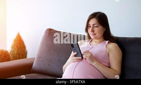 Femme enceinte se détendant sur un canapé en utilisant son smartphone Banque D'Images