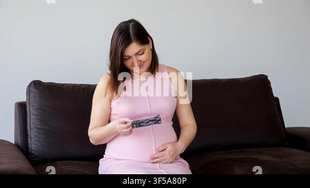 Femme enceinte regardant une échographie sur le canapé Banque D'Images