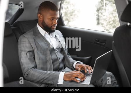 Un entrepreneur afro-américain prospère travaillant sur un ordinateur portable en voiture Banque D'Images