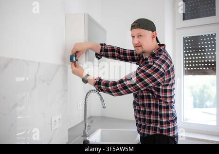 Un homme vérifie le niveau d'un placard mural avec un appareil laser lors d'un projet de rénovation de cuisine à domicile Banque D'Images
