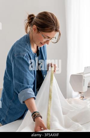 Artisane mesure avec précision un long tissu blanc pour un projet de vêtement. Banque D'Images