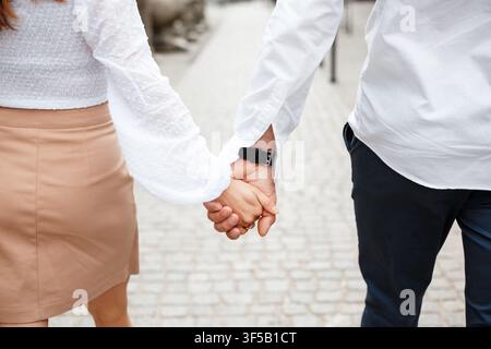 Un gros plan des mains d'un jeune couple marchant ensemble dans une rue ensoleillée. Concept de romance, de lien, de rencontres urbaines, de compagnonnage et d'amour moderne Banque D'Images