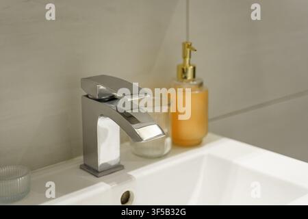 Robinier chrom moderne dans une salle de bain avec distributeur de savon. Robinier chrom moderne dans une salle de bain à côté d'un distributeur de savon sur un comptoir de lavabo propre. La scène met en avant l'hygiène, le style de la salle de bain Banque D'Images
