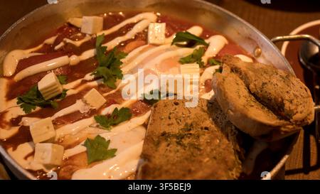 Shakshuka dans une poêle avec du fromage feta, une vinaigrette au yaourt et du pain grillé aux graines — concept : petit-déjeuner moyen-oriental, plat réconfortant, repas au restaurant, Banque D'Images