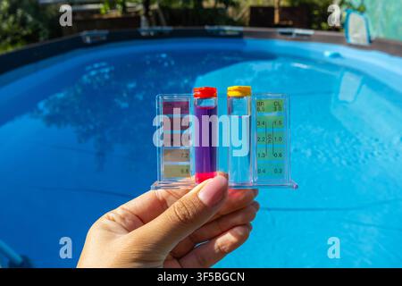 Un plan horizontal en gros plan d'une main tenant un kit de test du pH et du chlore de l'eau en plastique transparent rempli de réactifs liquides colorés au-dessus de clea Banque D'Images