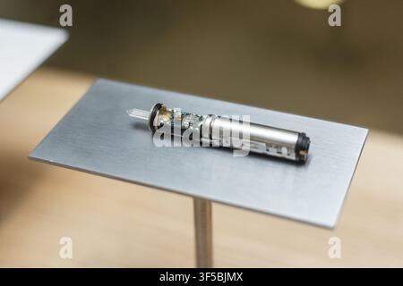 Petit composant cylindrique de capteur électronique d'une cigarette électronique sur une plateforme métallique grise dans un laboratoire. Recherche et développement de la technologie de vapotage, tests de contrôle qualité, ingénierie matérielle Banque D'Images