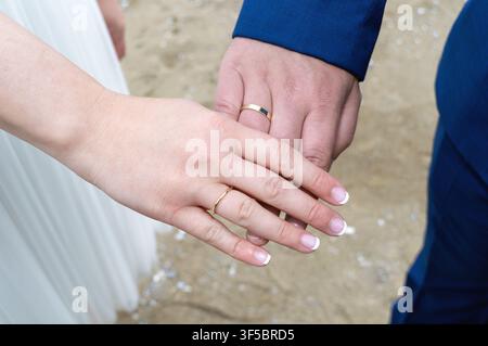 Close up de deux mains portant des alliances qui se touchent. Focus sur les doigts et les bagues en or avec un fond doux. Convient pour des thèmes comme le mariage Banque D'Images
