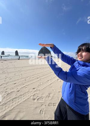 Femme posant de manière ludique sur la plage de sable près de Haystack Rock à Cannon Beach, Oregon, États-Unis. Banque D'Images