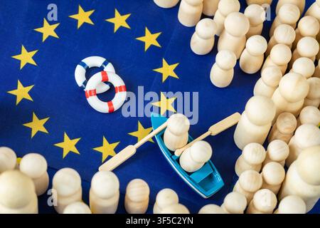 Concept de crise migratoire de l'UE avec un petit bateau, des bouées de sauvetage et des figurines en bois sur le fond du drapeau de l'Union européenne. Route des réfugiés en Méditerranée et frontière Banque D'Images