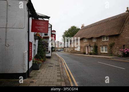 Une scène de rue tranquille dans le village d'Exton, Rutland, mettant en vedette un pub anglais traditionnel avec des panneaux oscillants face à des cottages historiques au toit de chaume. Banque D'Images