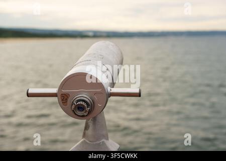 Téléscope touristique fonctionnant à la pièce, stationnaire, surplombant un horizon côtier calme et gris, point de vue public du front de mer, plateforme d'observation au bord de la mer, équipement optique maritime, tourisme côtier Banque D'Images