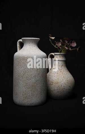 Deux vases en céramique rustiques tachetés avec anses sur fond noir Banque D'Images