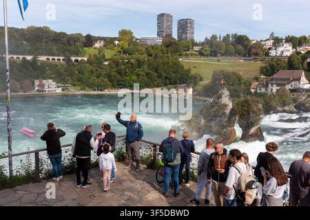 NEUHAUSEN, SUISSE - 13 SEPTEMBRE 2025 : Un groupe divers de touristes prenant des photos et profitant d'une puissante cascade qui dévale depuis une plateforme d'observation Banque D'Images