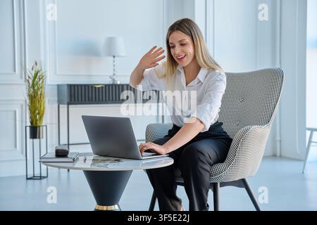 Jeune femme souriante en appel vidéo sur ordinateur portable dans un espace de bureau moderne Banque D'Images