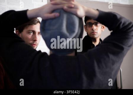 Deux membres de l'équipe surveillent le tournage les mains levées au-dessus de la tête d'un homme pendant la production du court-métrage britannique The Listener à Peckham Rye, Londres, Banque D'Images