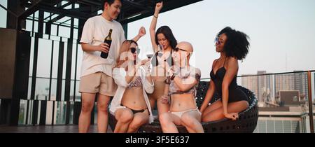 Amis divers portant un toast avec des verres de vin, célébrant une fête d'été au bord de la piscine sur le toit Banque D'Images