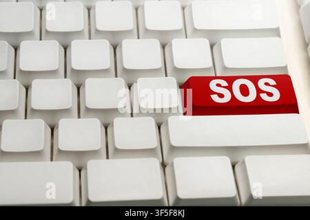 Un gros plan d'un clavier d'ordinateur blanc avec un seul bouton rouge étiqueté SOS, symbolisant un signal d'urgence numérique, une aide d'urgence ou technique Banque D'Images