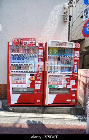 Deux distributeurs automatiques rouges de Coca-Cola debout côte à côte contre un mur de bâtiment sur un trottoir urbain au Japon. Banque D'Images
