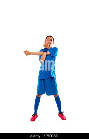 Portrait en pleine longueur d'un jeune homme indonésien d'Asie du Sud-Est en uniforme de football bleu effectuant un étirement des épaules avant l'entraînement, isolé sur un w Banque D'Images