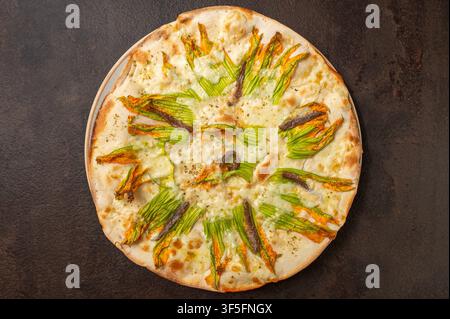 Pizza blanche italienne traditionnelle garnie de fleurs de courgettes, d'anchois et de mozzarella fondu, photographiée de dessus sur un fond rustique sombre Banque D'Images