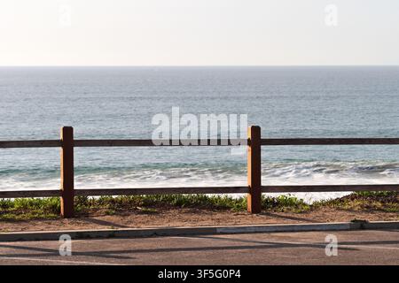 Clôture en bois le long d'une vue côtière avec des vagues de l'océan et un horizon clair sous la lumière chaude de Californie. Banque D'Images
