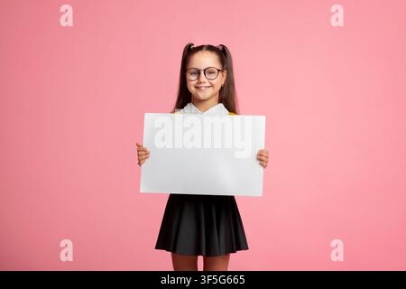 Gaie enfant écolière en uniforme et verres tient l'affiche avec espace vide Banque D'Images