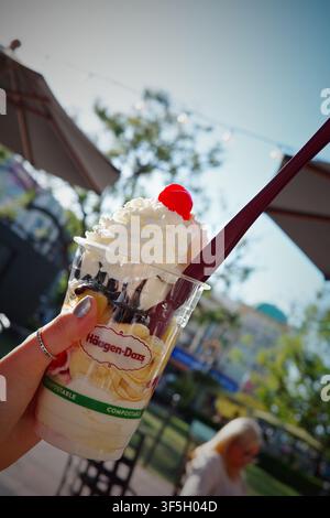 Main tenant un sundae glacé Häagen-Dazs avec de la crème fouettée et une cerise en extérieur Banque D'Images