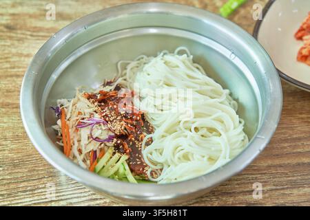 Bibim guksu, nouilles froides coréennes épicées avec légumes et sauce au piment, une collation de rue populaire que l'on trouve sur les marchés coréens. Banque D'Images