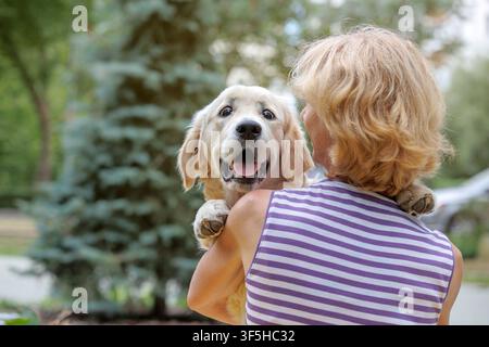 Femme souriante tenant un adorable chiot Golden Retriever en plein air. Propriétaire de chien heureux embrassant son jeune chien dans le parc. Lien fort entre l'homme et l'animal, compagnie Banque D'Images