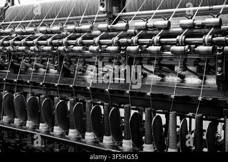 Moulinet de filage industriel vintage dans une usine textile historique, rangées de bobines de filage, production de fil de laine, machines textiles antiques, noir. Banque D'Images