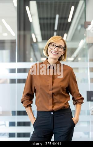 Professionnel heureux debout avec assurance dans un cadre de bureau contemporain, incarnant le leadership et le succès tout en regardant l'appareil photo Banque D'Images