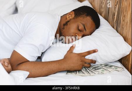 Black Man Sleeping Hiding Money sous l'oreiller dans le lit à l'intérieur Banque D'Images