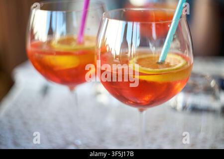 Deux verres à vin élégants remplis d'un cocktail aperitif orange vif garni de tranches d'agrumes fraîches et de pailles colorées. Banque D'Images