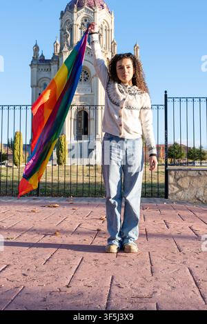 Jeune femme brandissant un drapeau de la fierté devant une église Banque D'Images