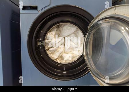 Grossissement d'une machine à laver à chargement frontal ouverte avec du linge blanc dans le tambour, montrant la porte en verre et le bord métallique dans une buanderie moderne Banque D'Images
