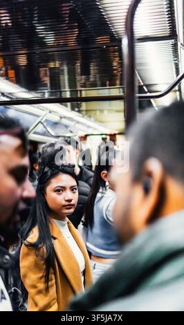 Une femme portant un manteau élégant se tient dans un métro bondé, immergée dans l'atmosphère urbaine animée. La scène capture le rythme dynamique de la ville Banque D'Images