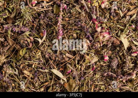 Texture en gros plan d'un mélange de thé à base de plantes séché comprenant des feuilles vertes, des tiges et des pétales de fleurs roses et violets. Fond botanique naturel pour bienne Banque D'Images