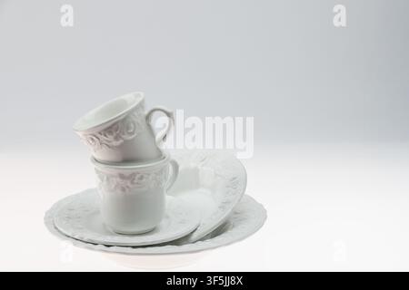 Nature morte minimaliste en studio de deux tasses en céramique blanches ornées empilées sur une soucoupe placée du côté droit du cadre sur un fond gris. La décoration Banque D'Images