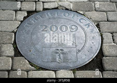 Une vue de dessus en gros plan d'une plaque métallique circulaire encastrée dans un pavé gris. Le disque métallique patiné arbore le texte cyrillique « ПЯТ» Banque D'Images
