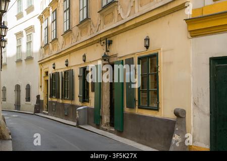 Une rue européenne étroite et déserte bordée de bâtiments traditionnels jaunes et de volets verts, capturée pour mettre en valeur l'atmosphère sereine et l'architecture Banque D'Images