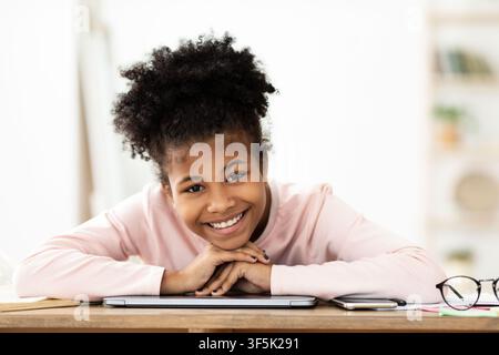 Gaie Black Teen Girl souriant assis au bureau à la maison Banque D'Images