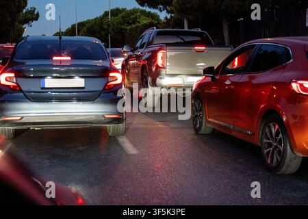 Vue arrière de voitures immobilisées dans un embouteillage nocturne sur une route urbaine en soirée, les feux de freinage lumineux se reflétant sur l'asphalte qui semble mouillé pendant l'heure de pointe Banque D'Images