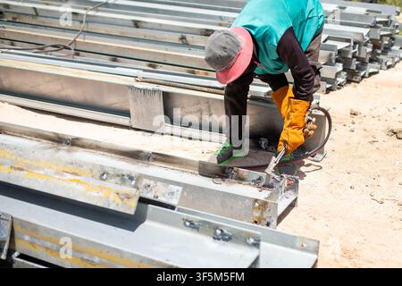 Ouvrier du bâtiment portant des gants de protection et coupant une poutre en I en acier avec un chalumeau à gaz oxy-combustible en plein air sur un chantier de construction Banque D'Images