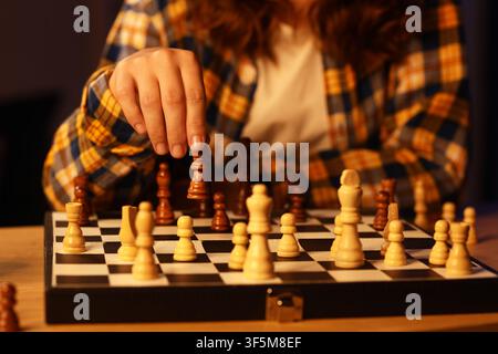 Personne en chemise à carreaux faisant un coup stratégique avec une pièce d'échecs sombre sur un échiquier lors d'une partie Banque D'Images