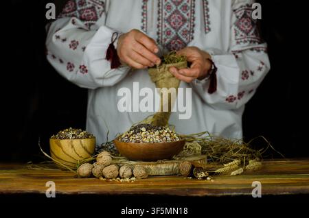 Femme en chemise brodée traditionnelle ukrainienne préparant un porridge rituel de blé de Noël à une table festive décorée. Banque D'Images