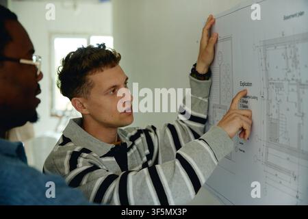 Hommes divers discutant d'un plan de rénovation de maison sur le mur Banque D'Images
