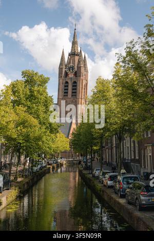 Vue de l'Oude Kerk, connue comme l'Église vieille, dominant une rue de canal pittoresque, avec des voitures garées et des arbres verts à Delft, Pays-Bas Banque D'Images